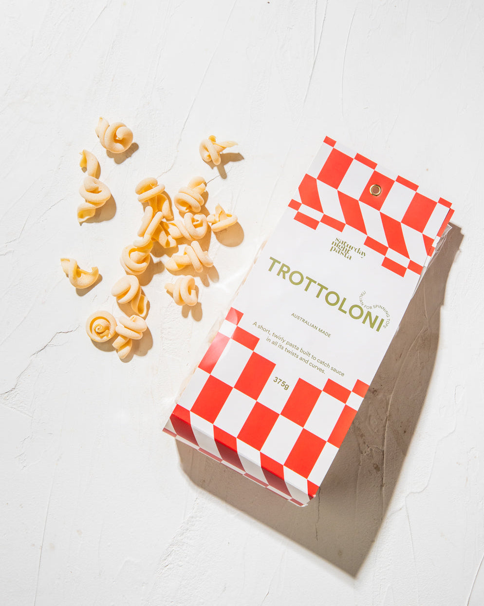 A box of dried Trottolini pasta with several pasta pieces scattered in front of it on a white surface.