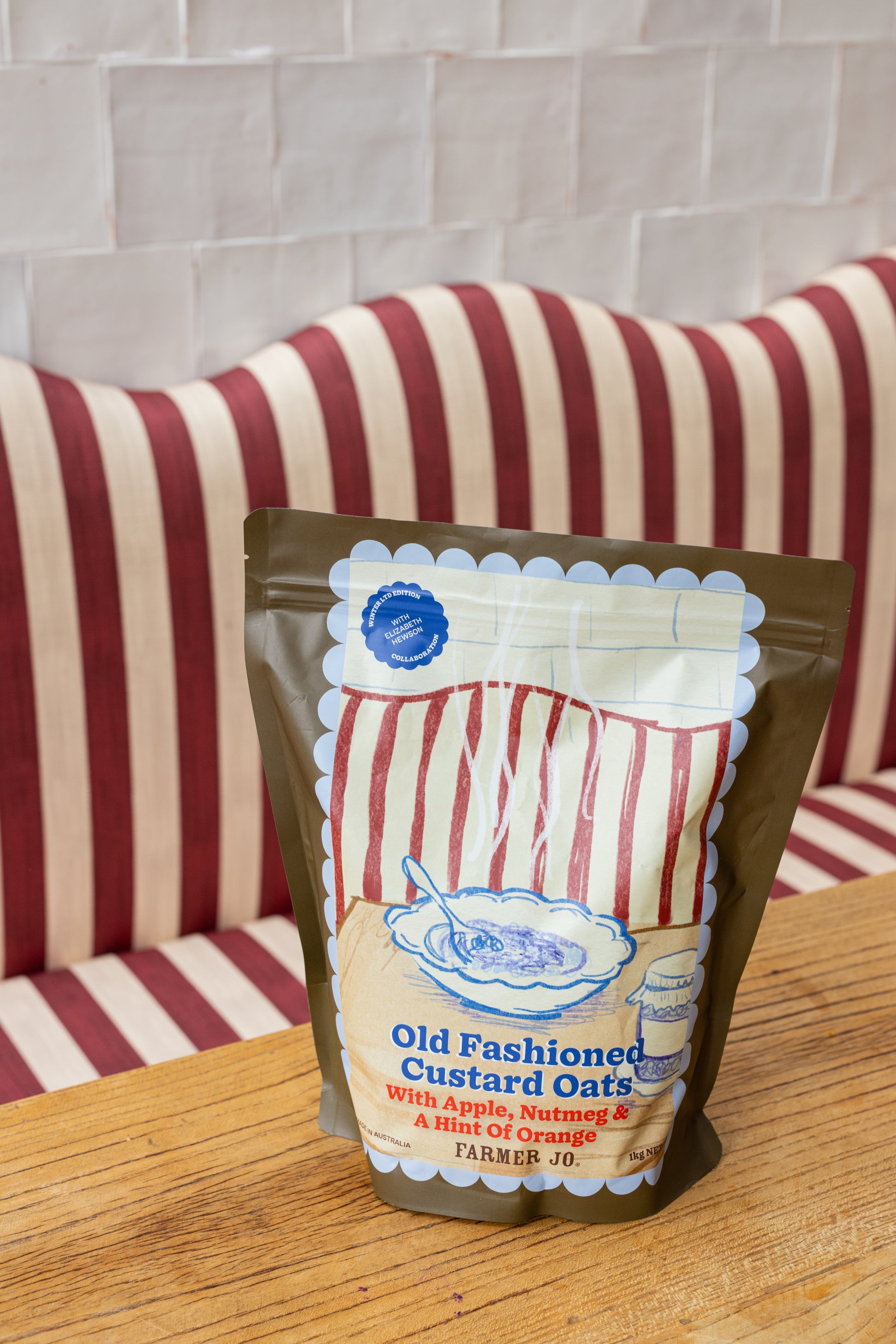 Packaged product labeled 'Old Fashioned Custard Oats' on a wooden surface with a striped cushion in the background.