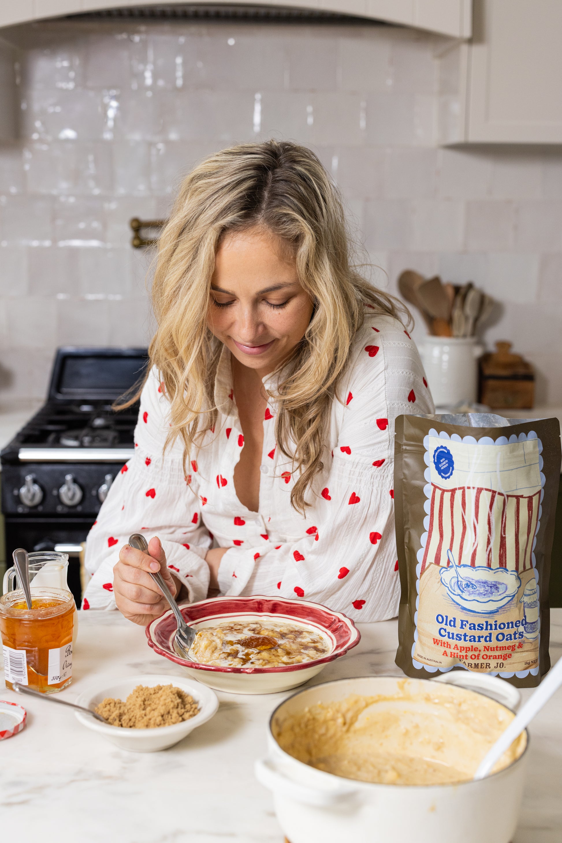 Woman in a kitchen eating oats with Old Fashioned Custard Oats packaging nearby.