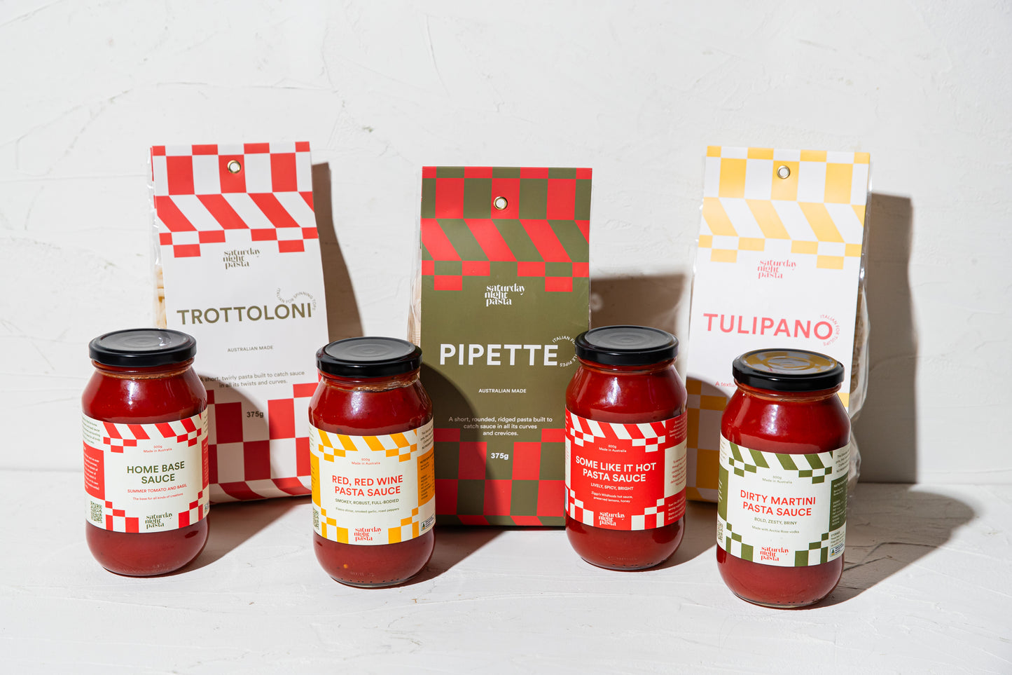 Four jars of pasta sauce and 3 packets of pasta with their packaging on a white background