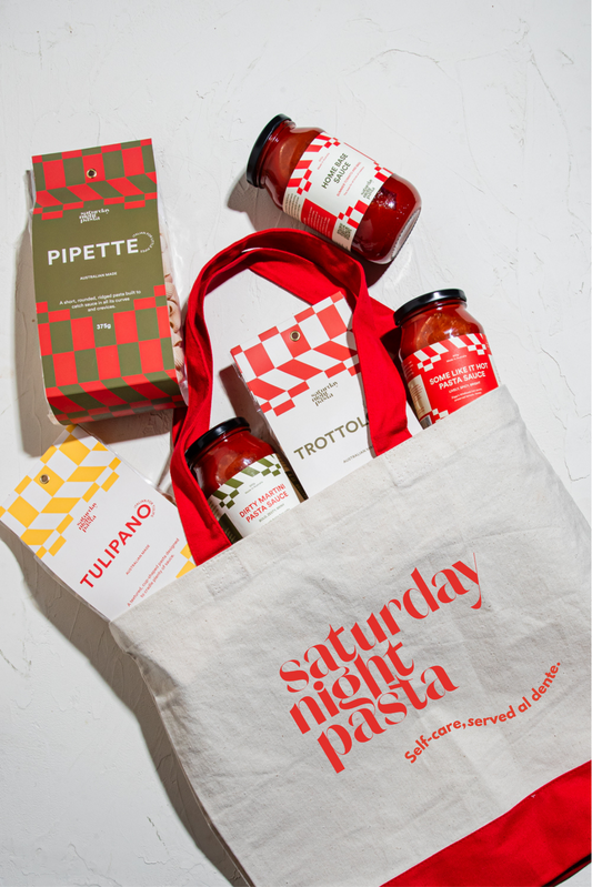 Tote bag with red text containing pasta sauce jars and pasta packets on a white background.