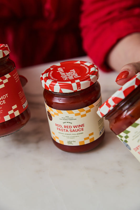 A jar of Red Red Wine Pasta Sauce on a white marble countertop, with a hand holding the lid and another jar partially visible on the left.